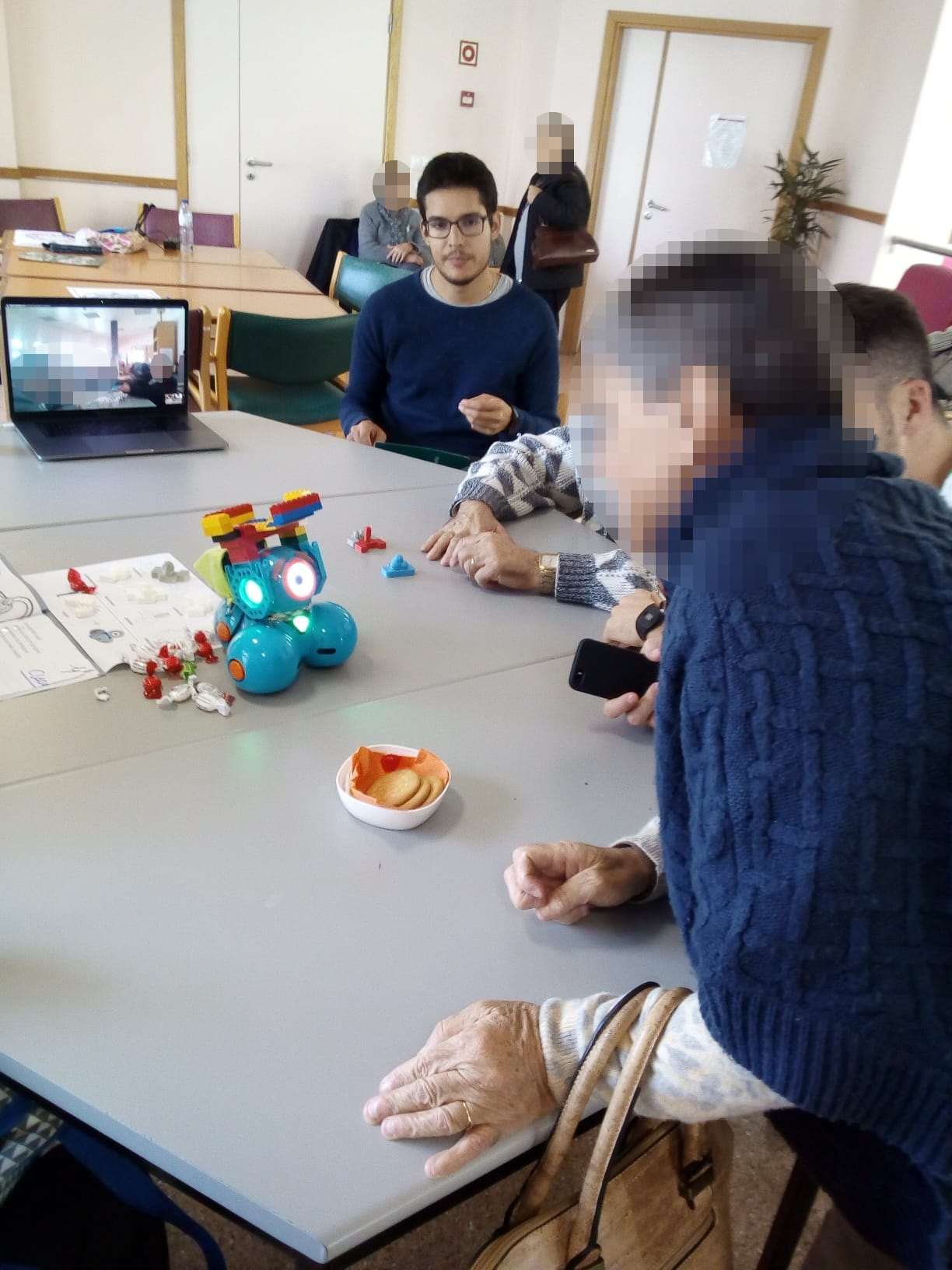 Photo taken from the Workshop with elderly people. Two people are interacting with the carrier robot