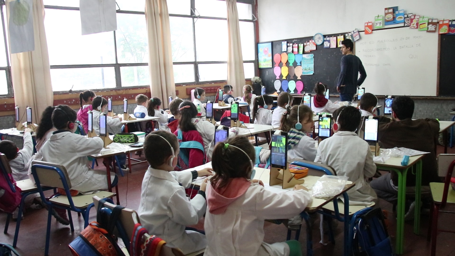 Photo taken during mathematics training with CETA system using tangibles. In this photo we observe an entire first grade classroom with 22 young children, playing with the blocks using our system CETA. Each child has a headphone, a tablet located on the table and the blocks to solve the additive composition tasks.